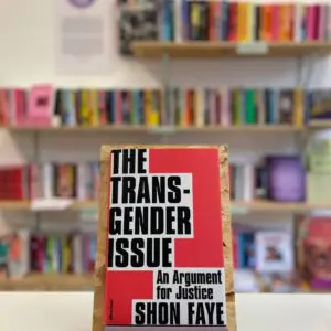 Cymraeg: Copi o 'The Transgender Issue' yn sefyll ar stondin llyfrau, tu blaen silffoedd o lyfrau yn y cefndir. English: A copy of 'The Transgender Issue' sits on a stand in front of multiple shelves of other books.