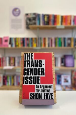 Cymraeg: Copi o 'The Transgender Issue' yn sefyll ar stondin llyfrau, tu blaen silffoedd o lyfrau yn y cefndir. English: A copy of 'The Transgender Issue' sits on a stand in front of multiple shelves of other books.