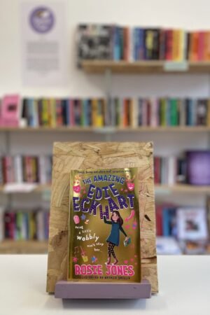 A copy of 'The Amazing Edie Eckhart' sits on a stand in front of multiple shelves of other books.