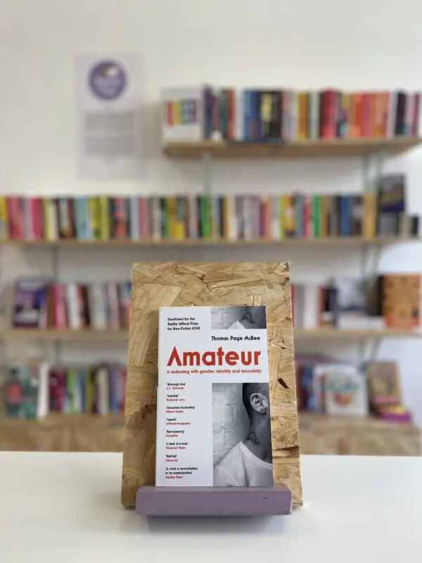 A copy of 'Amateur' sits on a stand in front of multiple shelves of other books.