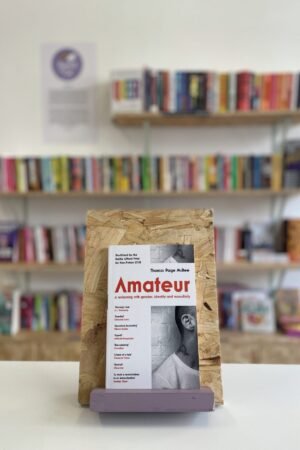 A copy of 'Amateur' sits on a stand in front of multiple shelves of other books.