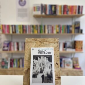 A copy of 'Women, Race & Class' sits on a stand in front of multiple shelves of other books.