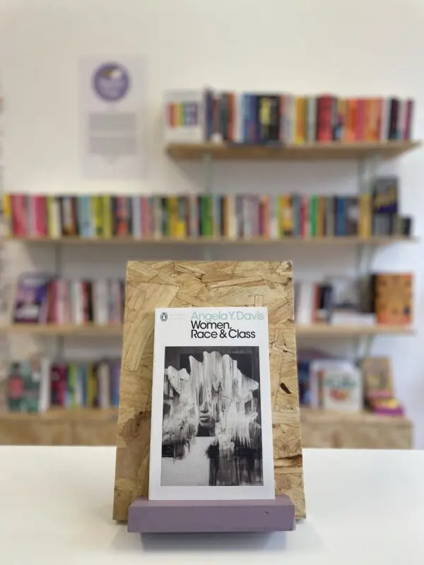 A copy of 'Women, Race & Class' sits on a stand in front of multiple shelves of other books.