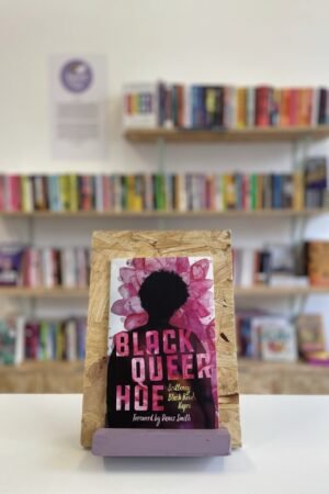 A copy o 'Black Queer Hoe' sits on a stand in front of multiple shelves of other books.
