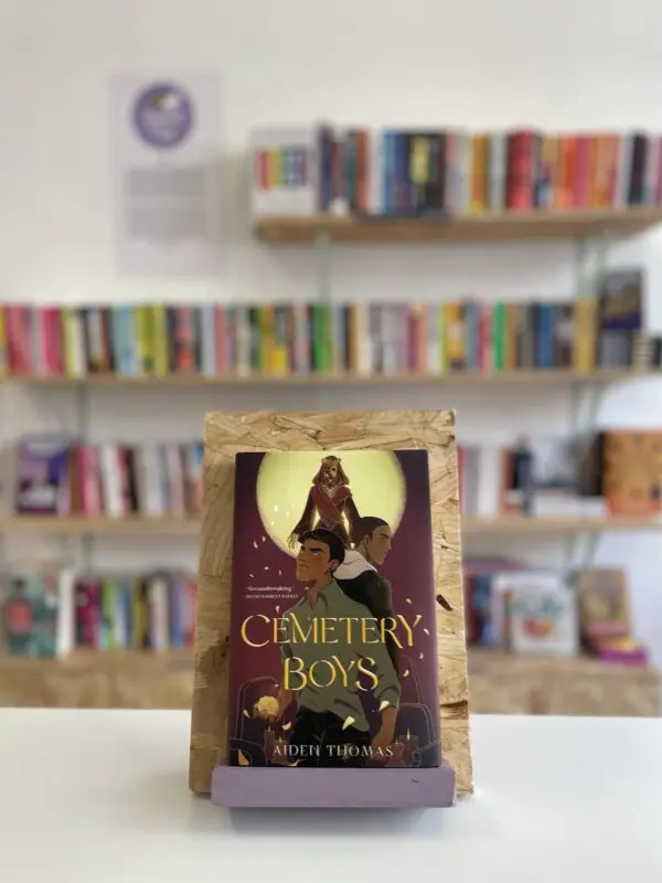 A copy of 'Cemetery Boys' sits on a stand in front of multiple shelves of other books.