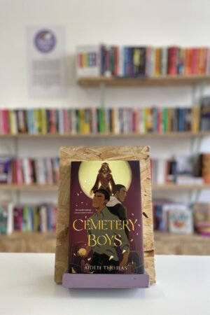 A copy of 'Cemetery Boys' sits on a stand in front of multiple shelves of other books.