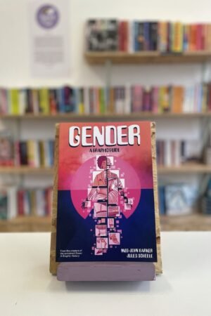 Cymraeg: Copi o 'Gender: A Graphic Guide' yn sefyll ar stondin llyfrau, tu blaen silffoedd o lyfrau yn y cefndir. | English: A copy of 'Gender: A Graphic Guide' sits on a stand in front of multiple shelves of other books.
