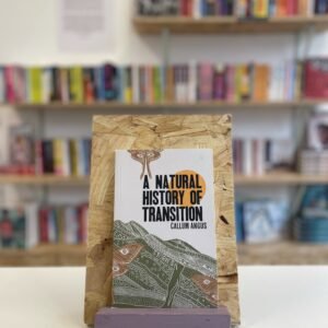 A copy of 'A Natural History of Transition' sits on a stand in front of multiple shelves of other books.