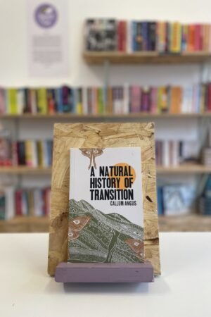A copy of 'A Natural History of Transition' sits on a stand in front of multiple shelves of other books.