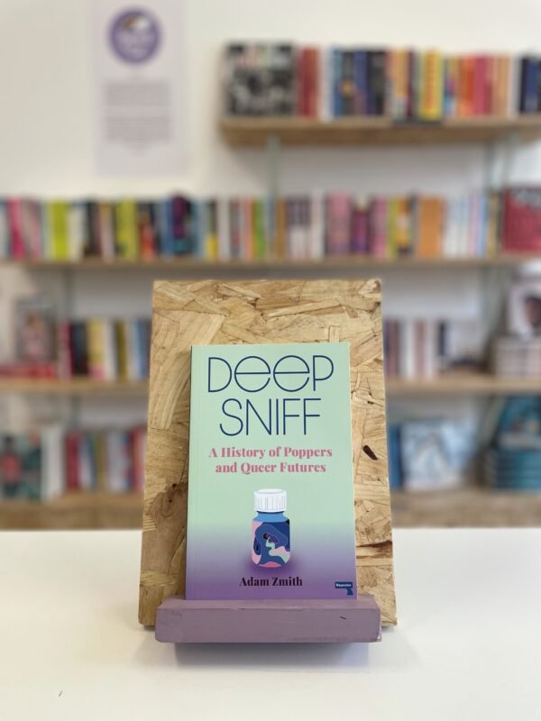 Cymraeg: Copi o 'Deep Sniff' yn sefyll ar stondin llyfrau, tu blaen silffoedd o lyfrau yn y cefndir. | English: A copy of 'Deep Sniff' sits on a stand in front of multiple shelves of other books.