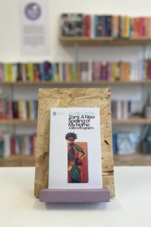 A copy of 'Zami' sits on a stand in front of multiple shelves of other books.