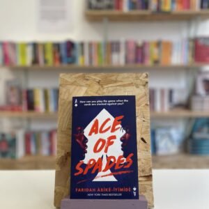 A copy of 'Ace of Spades' sits on a stand in front of multiple shelves of other books.