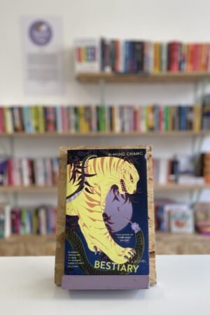 Copi o 'Bestiary' yn sefyll ar stondin llyfrau, tu blaen silffoedd o lyfrau yn y cefndir.