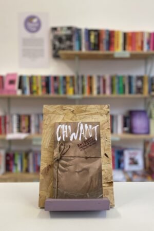 Cymraeg: Copi o 'Chwant' yn sefyll ar stondin llyfrau, tu blaen silffoedd o lyfrau yn y cefndir. | English: A copy of 'Chwant' sits on a stand in front of multiple shelves of other books.