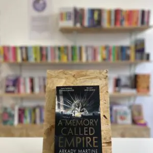 A copy of 'A Memory Called Empire' sits on a stand in front of multiple shelves of other books.