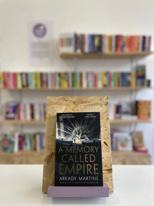 A copy of 'A Memory Called Empire' sits on a stand in front of multiple shelves of other books.