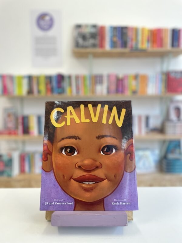 Cymraeg: Copi o 'Calvin' yn sefyll ar stondin llyfrau, tu blaen silffoedd o lyfrau yn y cefndir. | English: A copy of 'Calvin' sits on a stand in front of multiple shelves of other books.