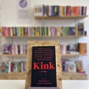 A copy of 'Kink' sits on a stand in front of multiple shelves of other books.
