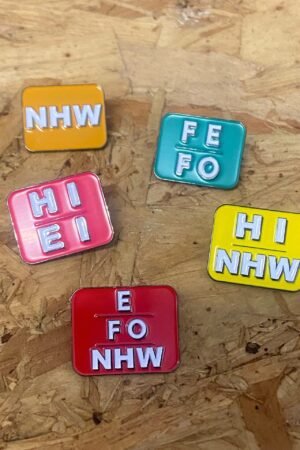 Cymraeg: Ar arwyneb pren, mae yna pump pin rhagenwau mewn lliwiau gwahanol: ‘E/Fe/Fo’ (coch/red) ‘Hi/Ei’ (pinc/pink) ‘Nhw’ (oren) ‘Fe/Fo’ (gwyrdd) ‘Hi/Nhw’ (melyn/yellow) English: The aforementioned Welsh language pronouns pins are sitting on a wooden surface.