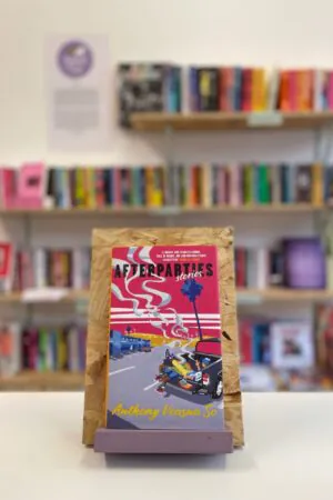 A copy of 'Afterparties' sits on a stand in front of multiple shelves of other books.