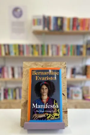 A copy of 'Manifesto' sits on a stand in front of multiple shelves of other books.