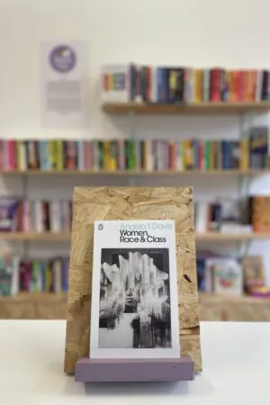 A copy of 'Women, Race & Class' sits on a stand in front of multiple shelves of other books.