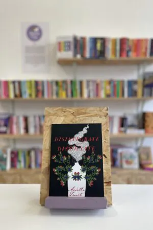 A copy of 'Disintegrate/Dissociate' sits on a stand in front of multiple shelves of other books.