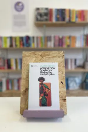 A copy of 'Zami' sits on a stand in front of multiple shelves of other books.