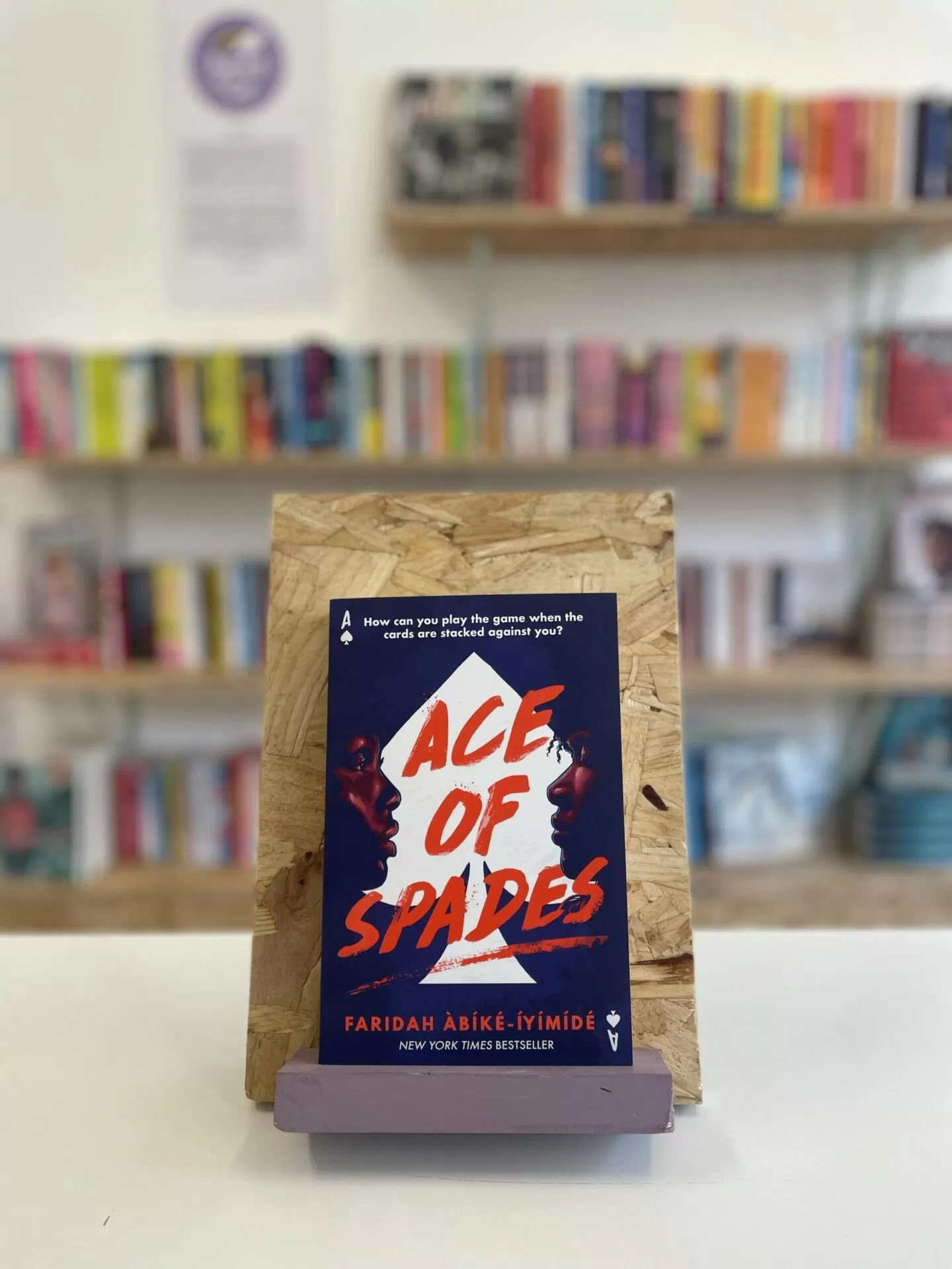 A copy of 'Ace of Spades' sits on a stand in front of multiple shelves of other books.