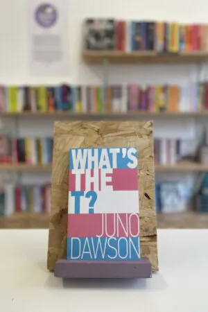 A copy of 'What's the T?' sits on a stand in front of multiple shelves of other books.