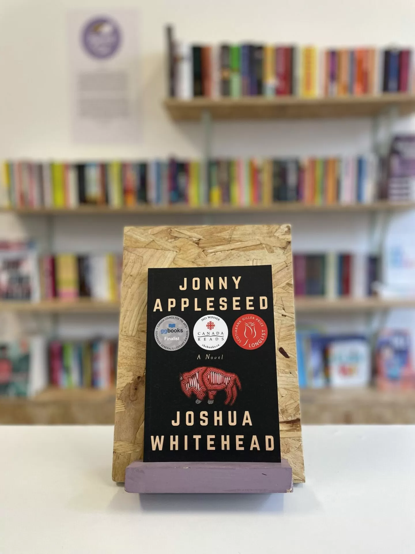 A copy of 'Jonny Appleseed' sits on a stand in front of multiple shelves of other books.