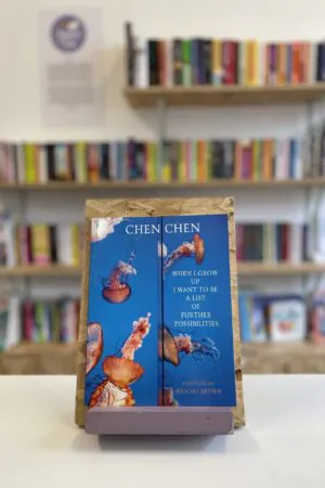 A copy of 'When I Grow Up I Want To Be A List of Further Possibilities' sits on a stand in front of multiple shelves of other books.