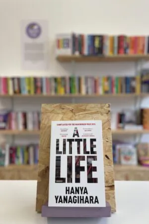 A copy of 'A Little Life' sits on a stand in front of multiple shelves of other books.