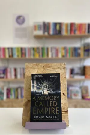 A copy of 'A Memory Called Empire' sits on a stand in front of multiple shelves of other books.
