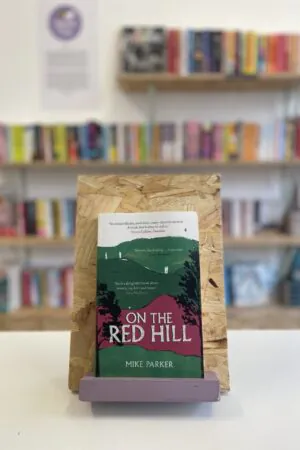 A copy of 'On the Red Hill' sits on a stand in front of multiple shelves of other books.