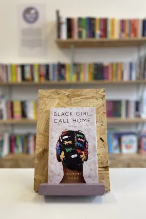 A copy of 'Black Girl, Call Home' sits on a stand in front of multiple shelves of other books.