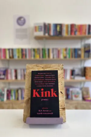 A copy of 'Kink' sits on a stand in front of multiple shelves of other books.