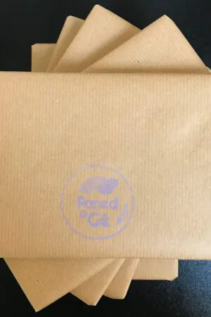 A pile of brown, square parcels on a black surface, asymmetrically arranged. Paned o Gê's logo is printed in lavender on the top parcel.